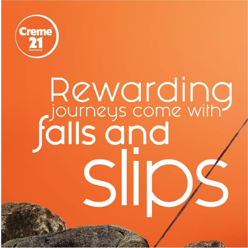 Creme 21 orange motivational poster with text "Rewarding journeys come with falls and slips" over rocky terrain.