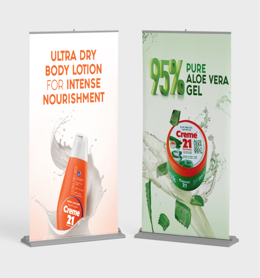 Two Creme 21 roll-up banners advertising ultra dry body lotion and 95% pure aloe vera gel with splash effects.