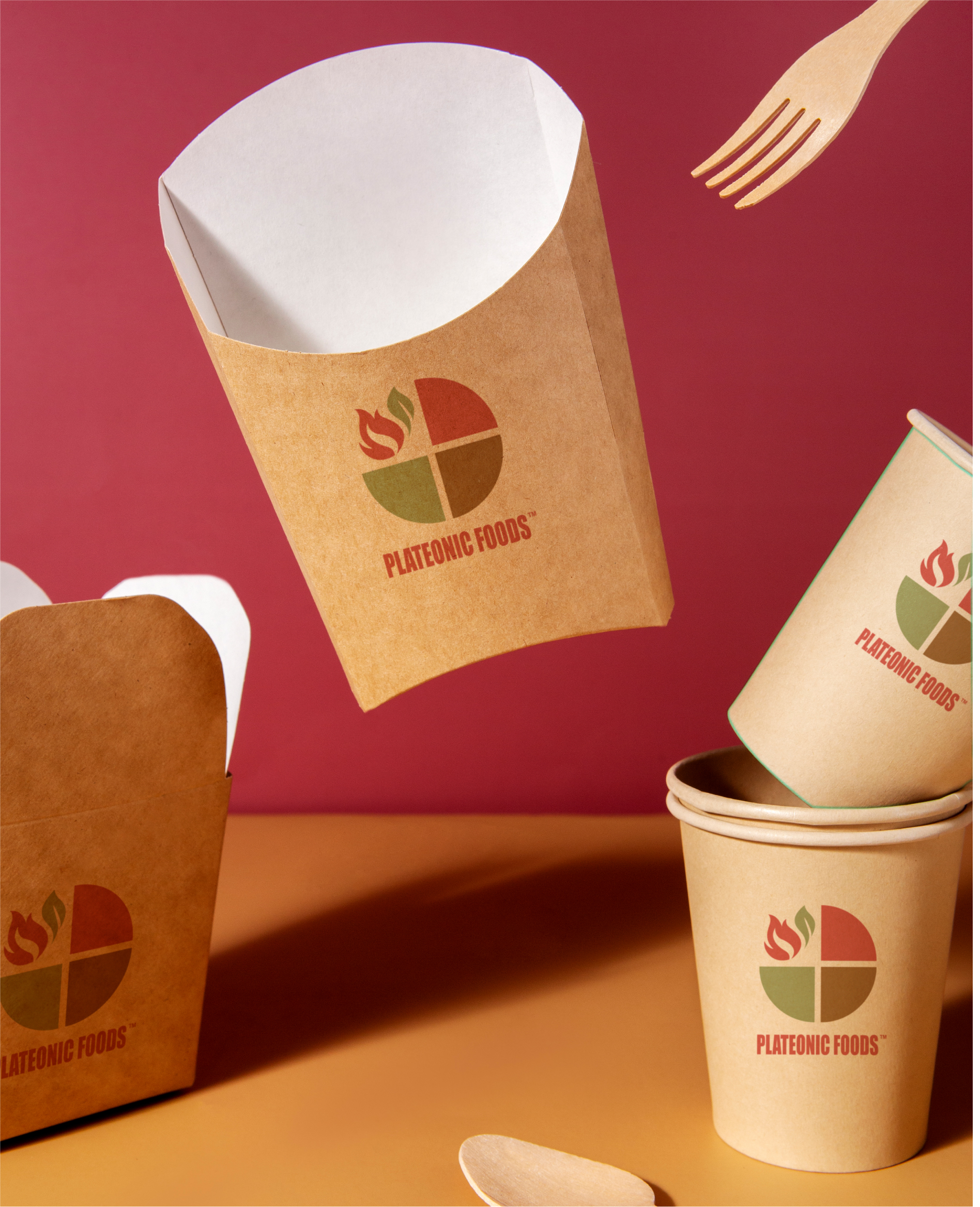 Plateonic Foods branded brown paper food containers, cups, wooden fork, and spoon on a red and yellow background.