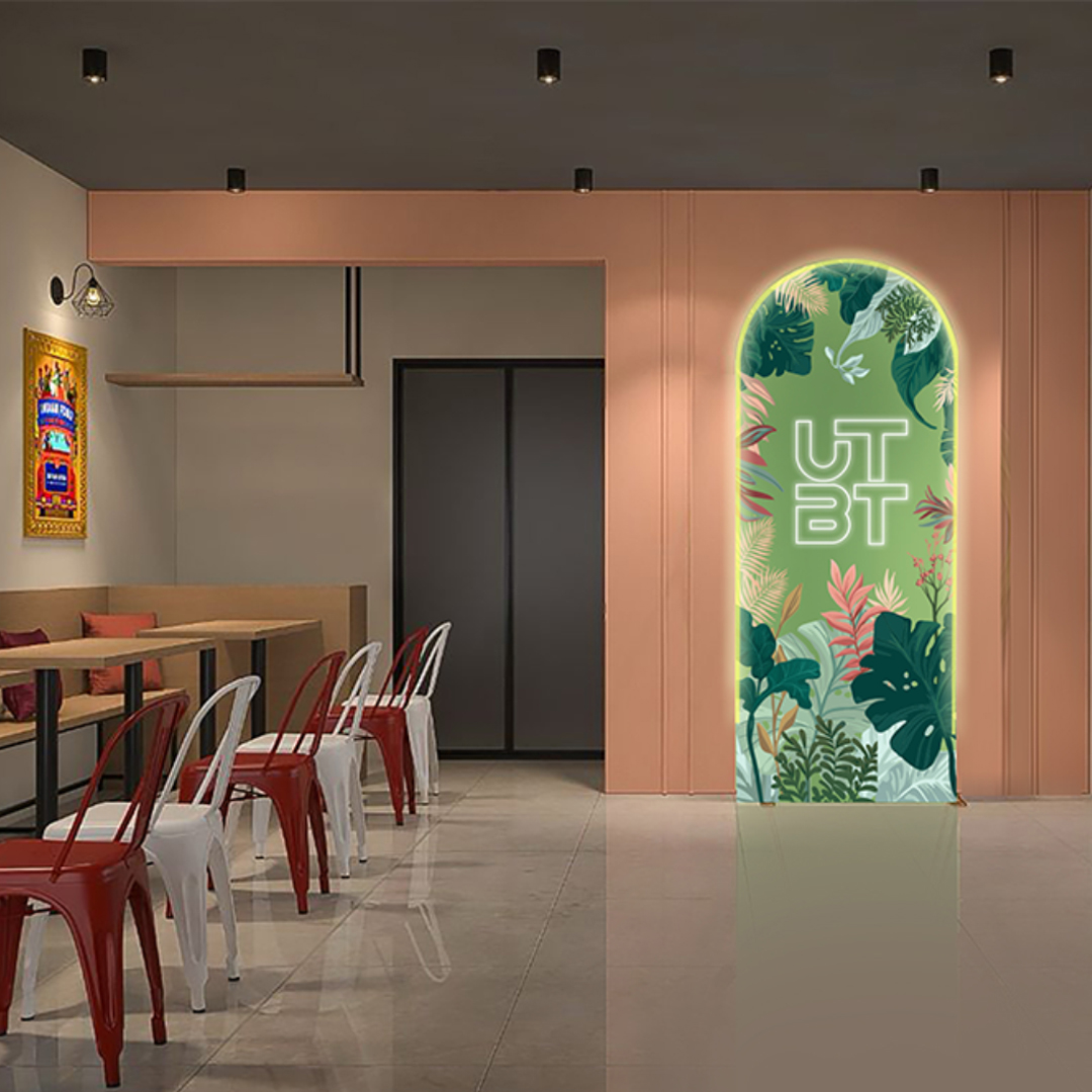 UTBT restaurant interior with red metal chairs, wooden tables, and illuminated tropical archway with brand logo