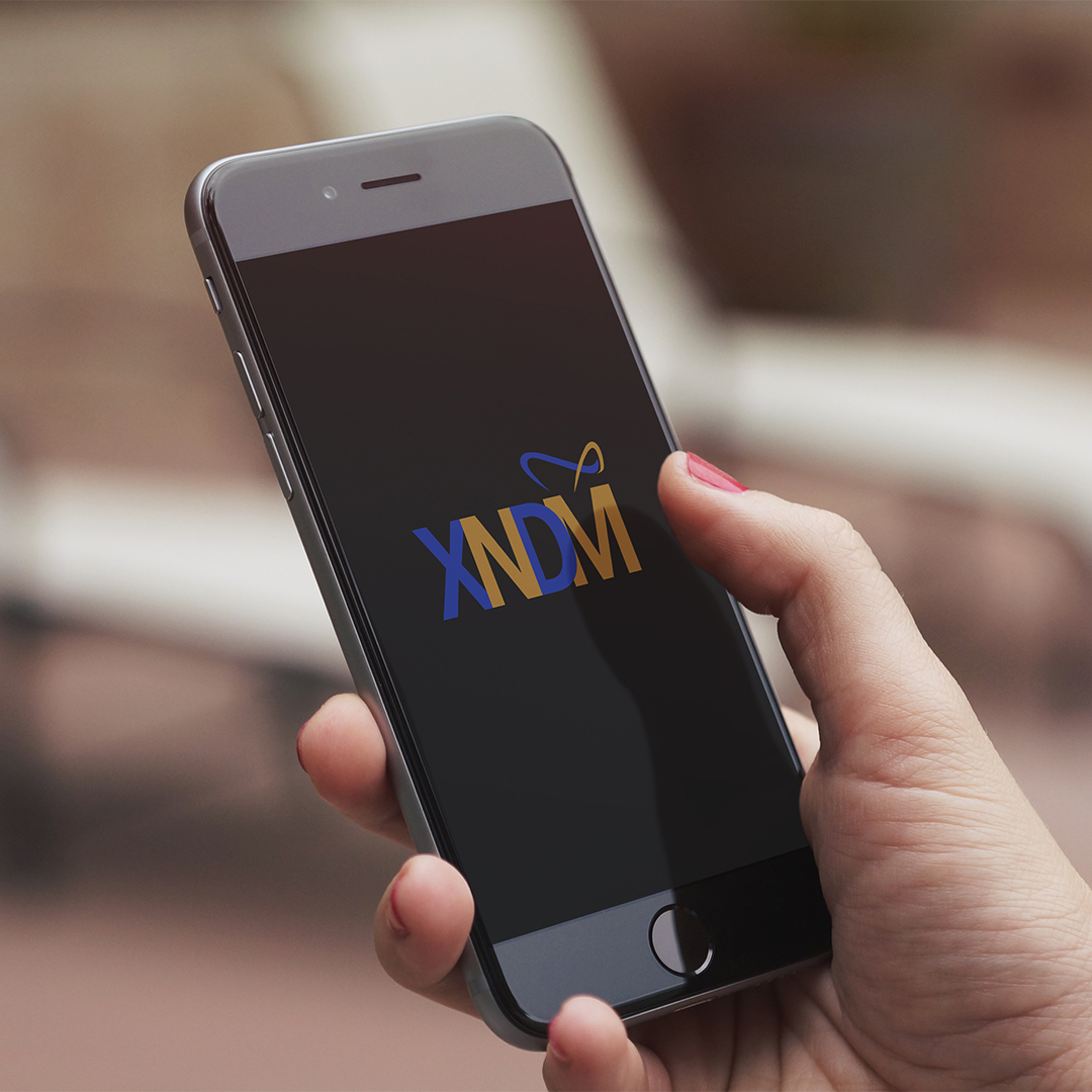 Hand holding smartphone displaying XNDM logo in blue and gold with decorative swoosh on black screen.