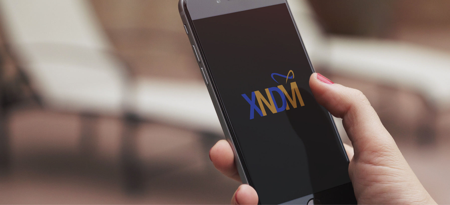 Smartphone displaying XNDM logo in blue and gold with decorative swoosh on dark screen, held in hand.