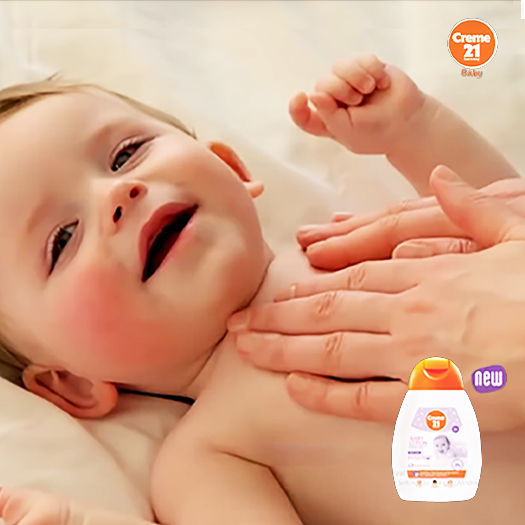 A parent gently applies Creme 21 Baby lotion to a baby's chest, with a bottle of the new lotion shown in the corner.