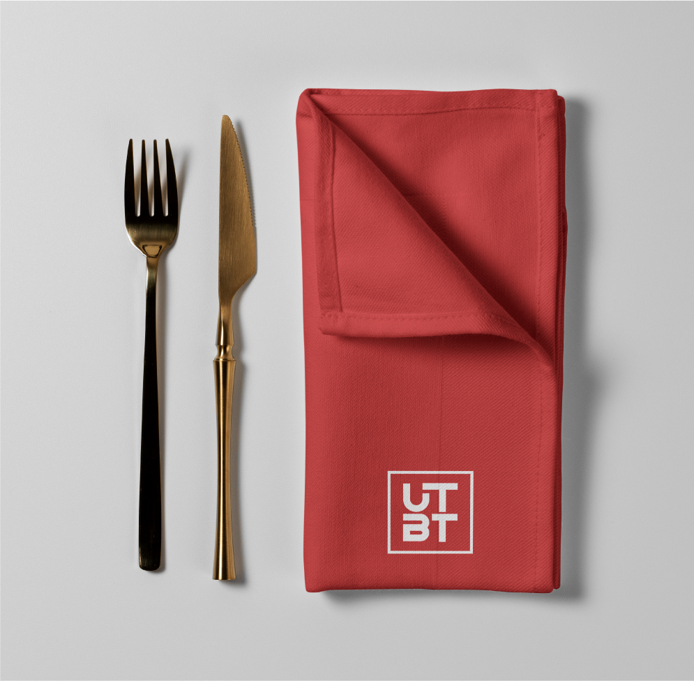 Gold fork and knife with red UTBT branded napkin arranged on light gray background for elegant table setting