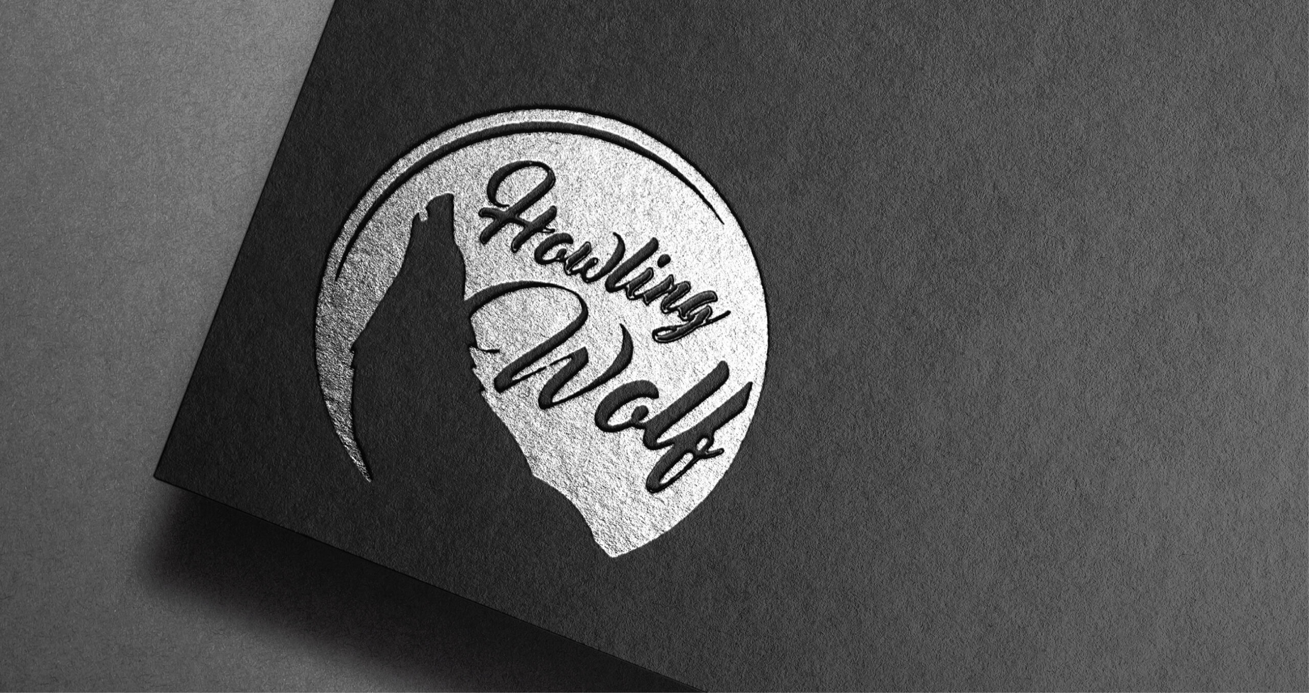 Metallic embossed Howling Wolf logo featuring a wolf silhouette and elegant script inside a circular design on black textured paper.