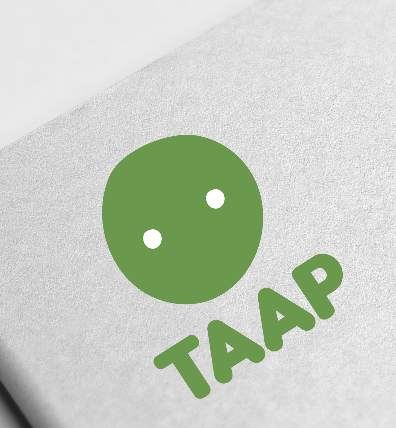 Green TAAP logo with a simple round face design and two white dots for eyes on a light textured background.