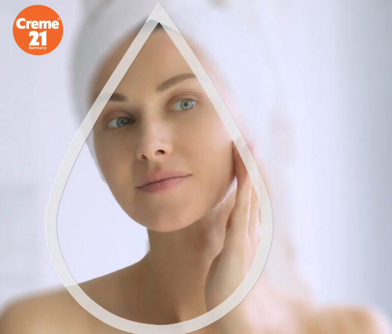 Creme 21 skincare advertisement with woman touching face framed by water droplet outline and orange logo.