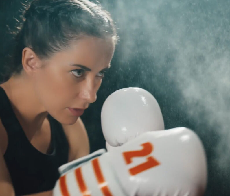 Woman with white boxing gloves training in gym with steam or dust effect in atmospheric lighting.