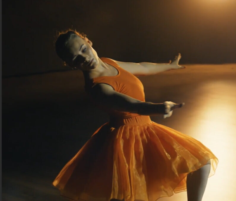 Woman in flowing orange dress dancing gracefully with dramatic lighting and motion blur effects.