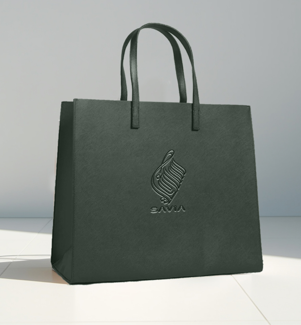 Elegant dark shopping bag with "SAVIA" logo and abstract emblem embossed on the front, standing on a light tiled floor.