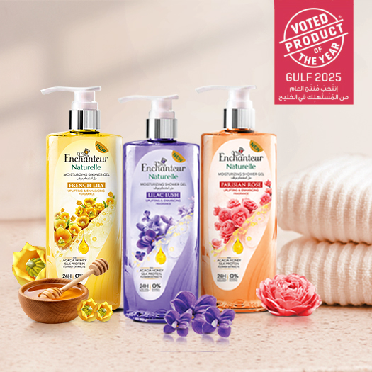 Three Enchanteur Naturelle shower gels French Lily, Lilac Lush, Parisian Rose displayed with flowers, honey, and towels.