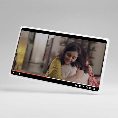 A video screen shows two people hugging in a cozy indoor setting with shelves in the background.