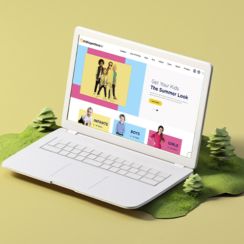 A white laptop displays a kidswear website with colorful sections for different age groups.
