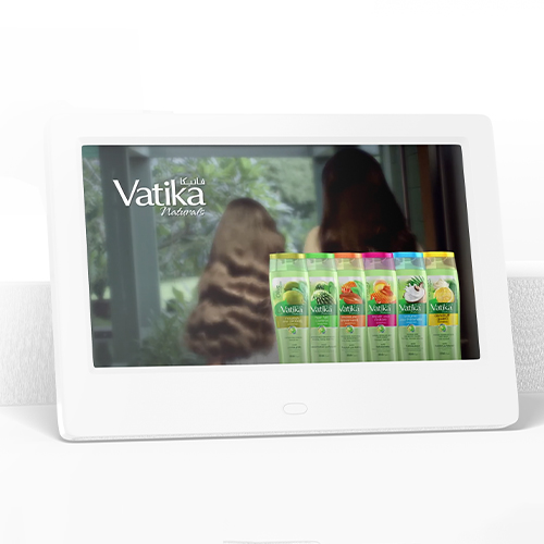 A digital screen displays Vatika Naturals shampoo bottles with two women showing their hair in the background.