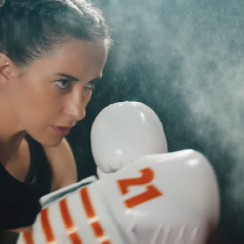 Boxer in black top wearing white gloves with orange stripes and number 21, preparing to fight.