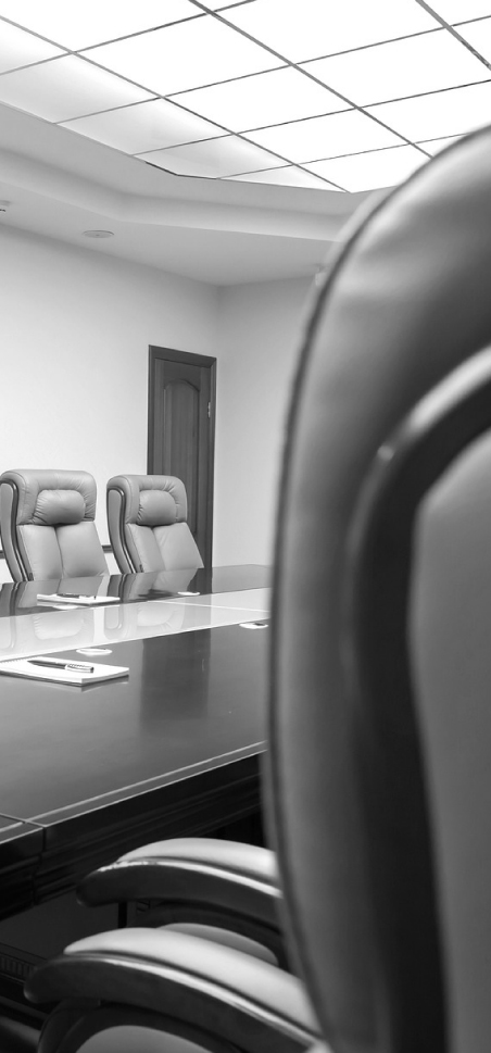 Monochrome photo of a modern conference room with leather chairs and a polished table under fluorescent lighting.