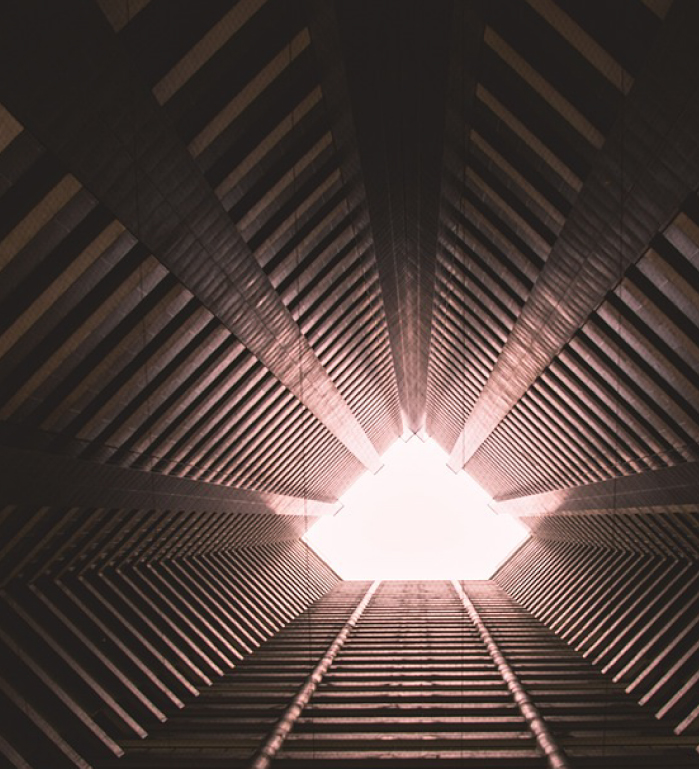 Symmetrical view looking up through a geometric, ribbed structure toward a bright opening at the top.
