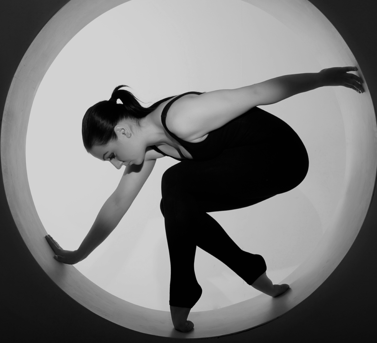 A woman in a black outfit balances gracefully inside a large circular frame, with arms and legs extended.