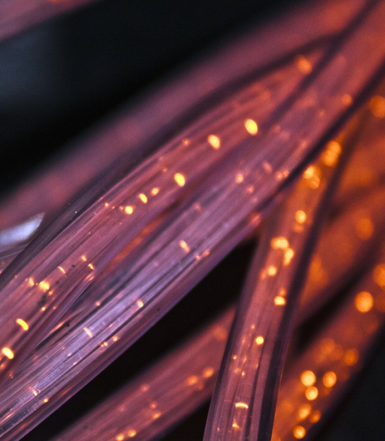 Close-up of glowing fiber optic cables with orange light dots against a dark background.