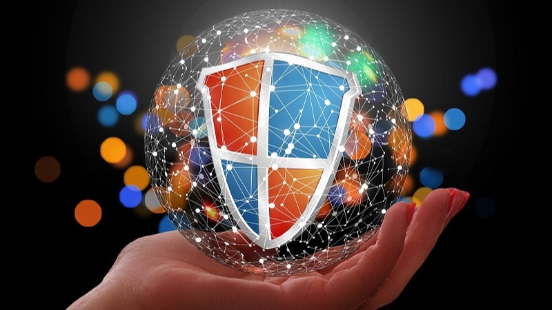 Hand holding a digital sphere with a shield icon and network connections, against a background of colorful bokeh lights.