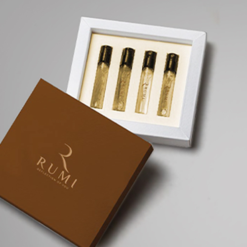 A brown RUMI box and a white frame display four gold perfume vials on a gray surface.